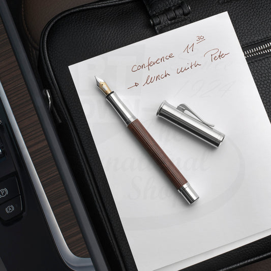 Graf von Faber-Castell Classic Grenadilla Fountain Pen with silver cap and brown wood barrel on white paper writing