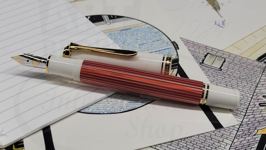 Pelikan Souveran M600 823111 fountain pen in red-striped cellulose acetate and white resin, gold-plated trim, rhodium-plated 14k nib, displayed on paper