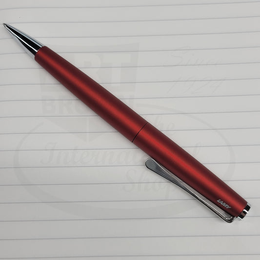 LAMY Studio L267RRM metal ballpoint pen in royal red matte finish with sleek cylindrical body and chrome clip, displayed on lined paper