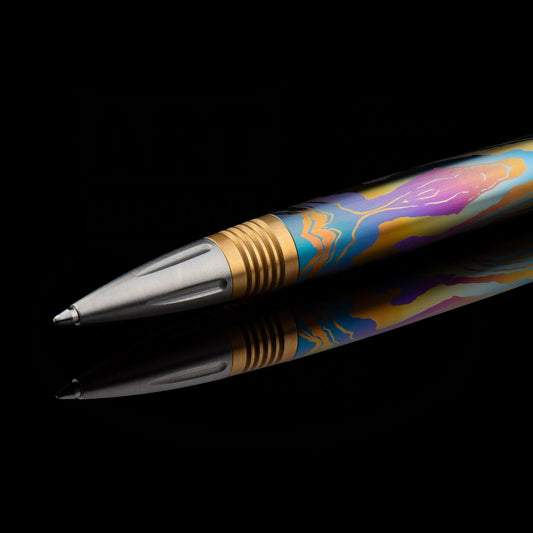 William Henry Caribe 8 titanium ballpoint pen with colorful anodized pattern, brass grip section, and stainless steel tip and top, displayed on reflective black surface