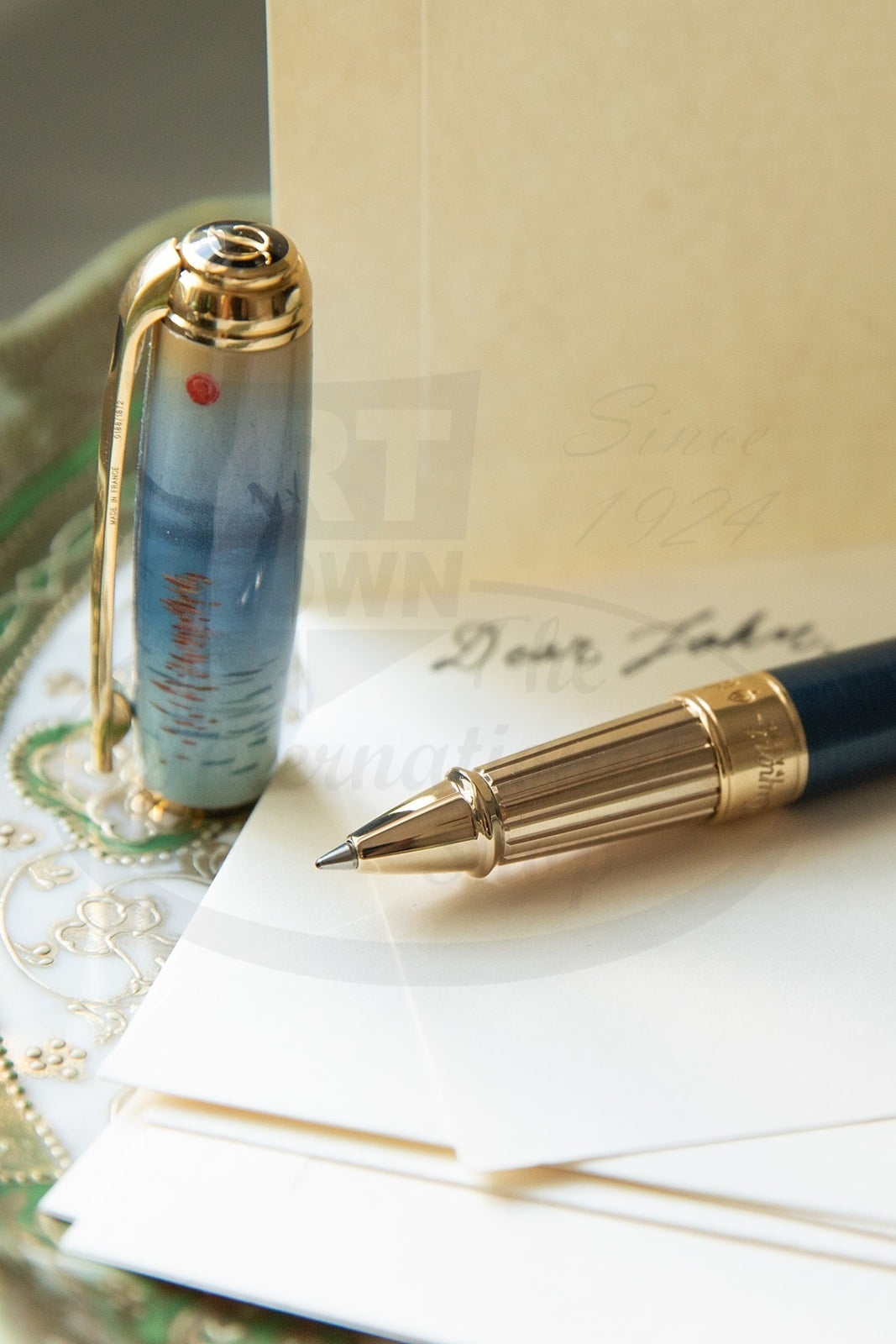 S.T. Dupont Line D 412049L rollerball pen featuring Monet's Impression Sunrise design on blue lacquered barrel with gold-plated palladium trim, displayed with writing paper