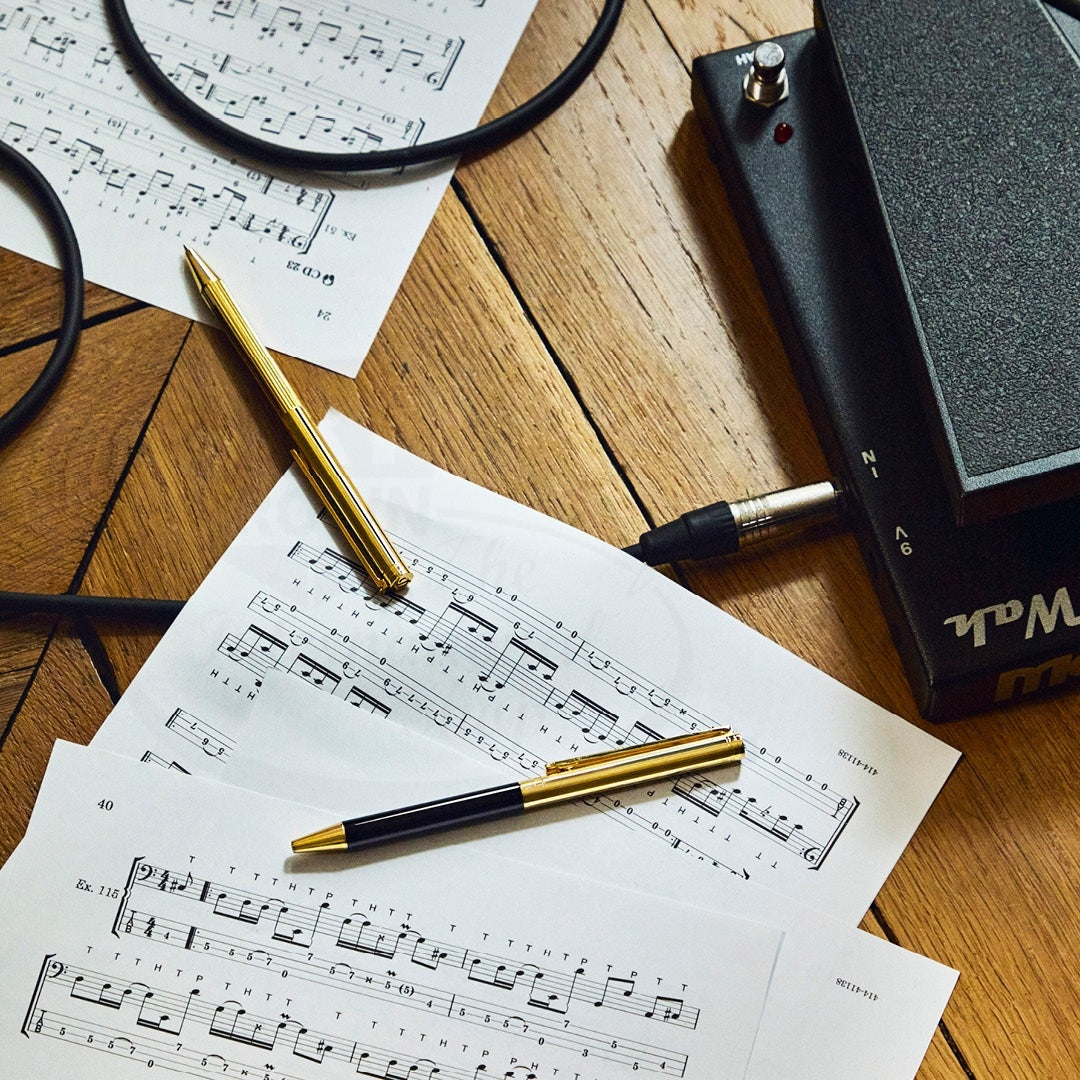 Gold and black executive ballpoint pens resting on musical sheets beside audio equipment on a wooden surface