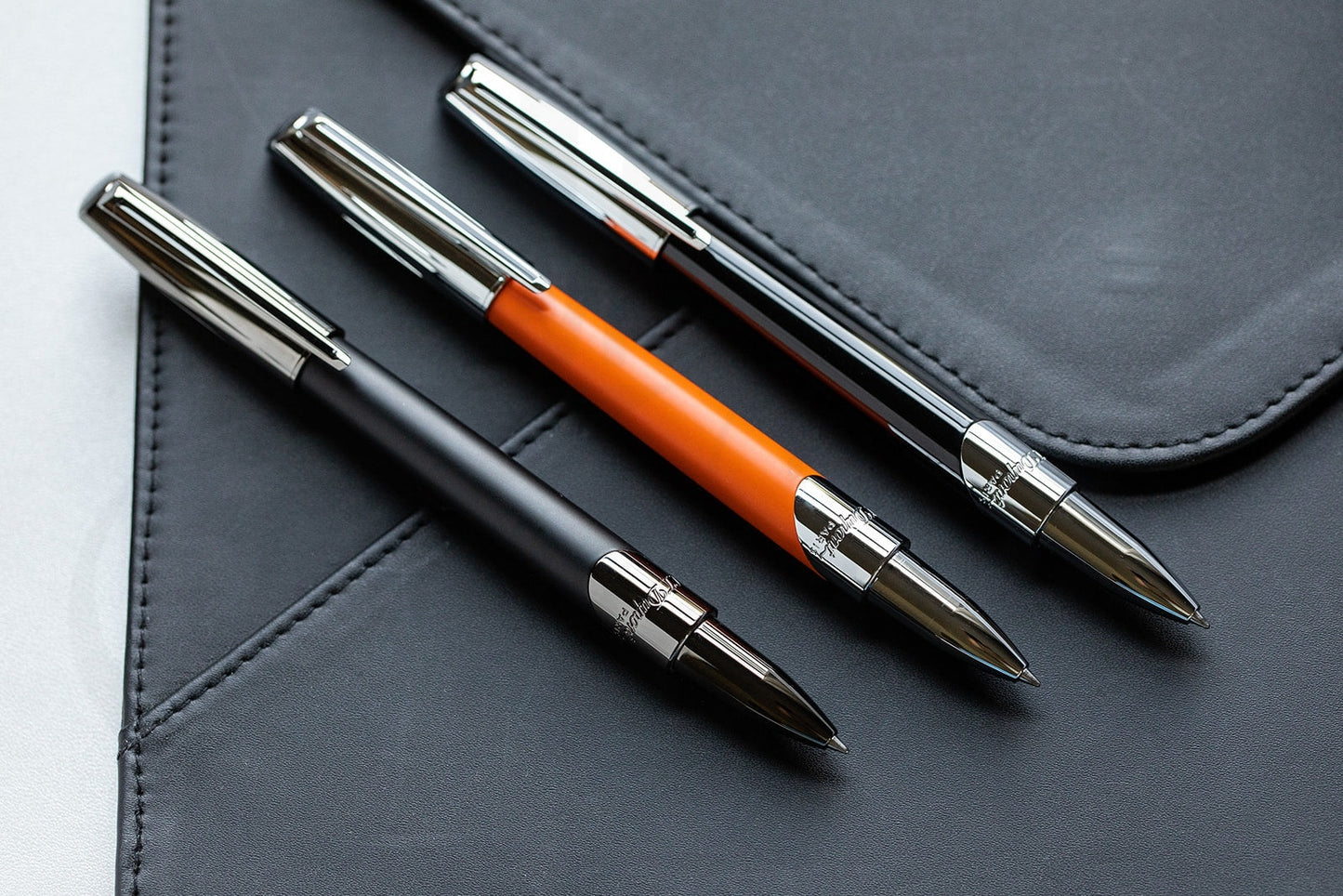S.T. Dupont Defi Millennium 402737 brass rollerball pens in silver chrome finish with matte orange and black barrels on leather surface