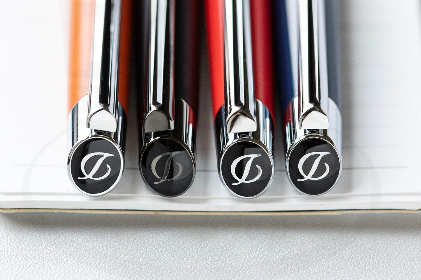 S.T. Dupont Defi Millennium 402003 rollerball pens in brass and lacquer, showing magnetic caps with Dupont logo, arranged in black, red, and chrome finishes