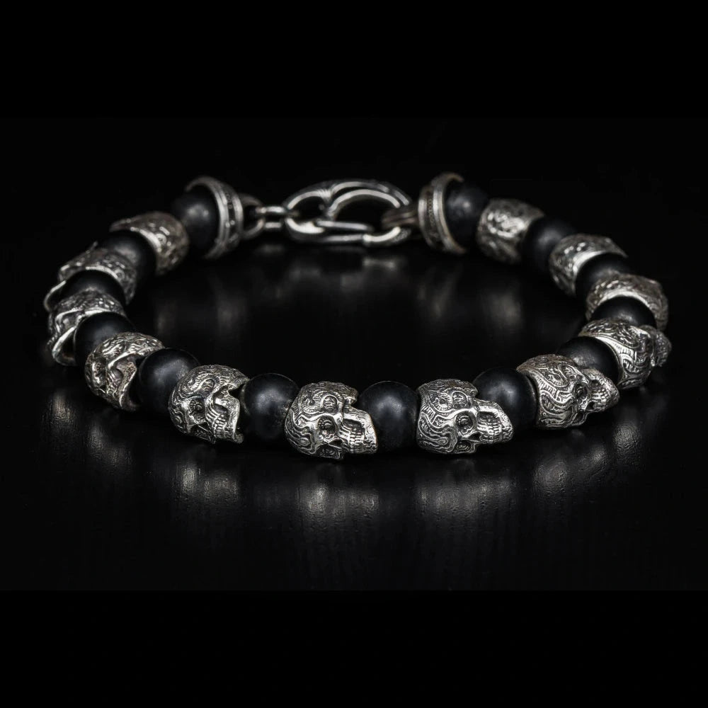 William Henry Shaman bracelet featuring sterling silver skull beads with intricate sugar skull designs alternating with 8mm black onyx beads, secured by silver clasp on black background