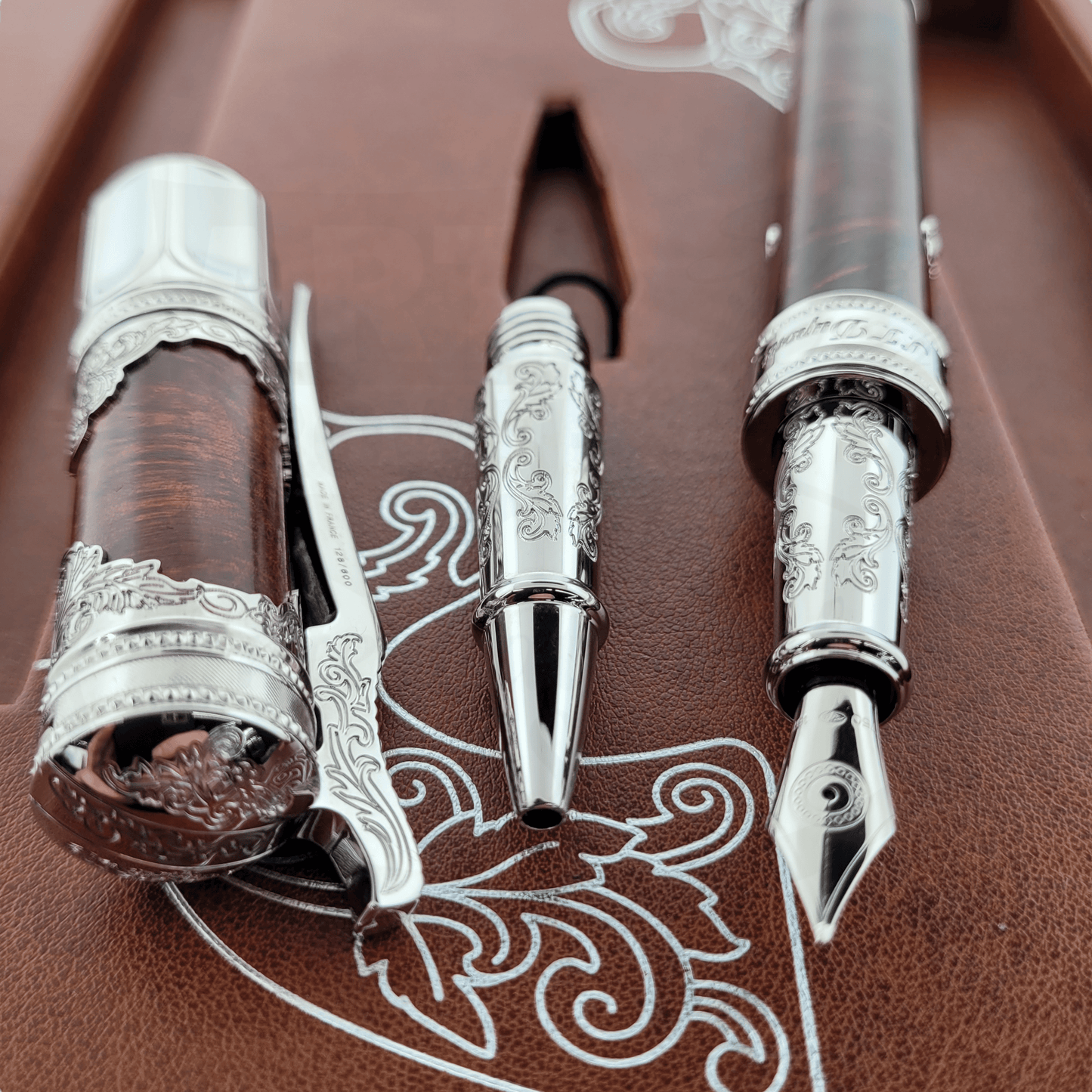 S.T. Dupont wild west premium engraved fountain pen, engraved rollerball convertor, and ornate cap laying side by side on brown display box