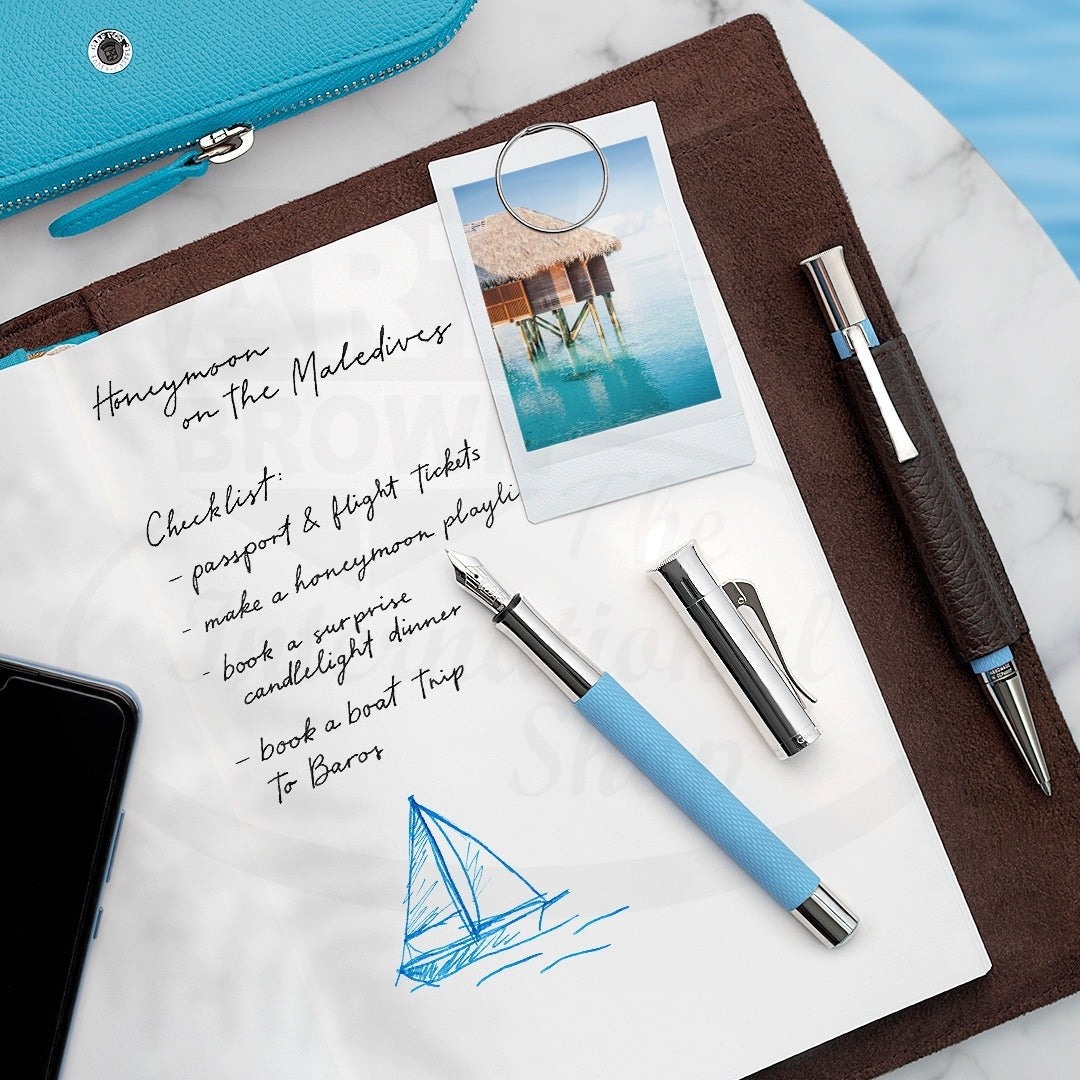 Graf von Faber-Castell Guilloche Blue Gulf fountain pen with resin barrel and silver accents, open with cap off on notebook