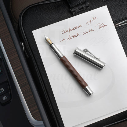 Graf von Faber-Castell Classic Grenadilla Fountain Pen with silver cap and brown wood barrel on white paper writing