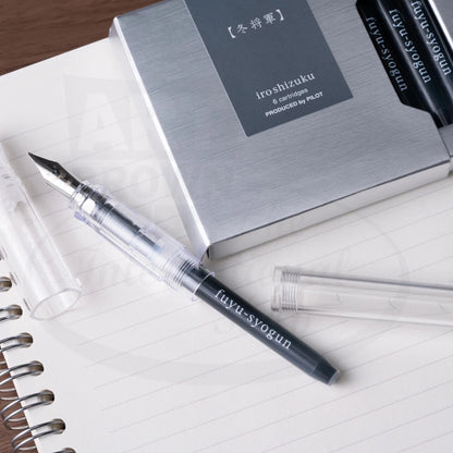 Pilot Iroshizuku 6-pack cartridges in silver box with transparent demonstrator fountain pen displaying black-gray ink on lined notebook paper
