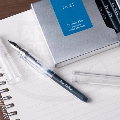 Pilot Iroshizuku cartridge 6-pack in blue packaging with silver metallic box, displayed alongside transparent fountain pen and clear ink cartridges on lined paper