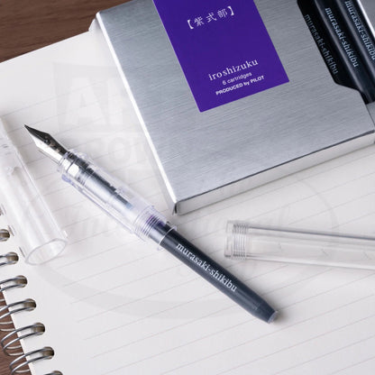 Pilot Iroshizuku plastic ink cartridge 6-pack in silver box with purple label, shown with transparent fountain pen and demonstrator cap on lined paper