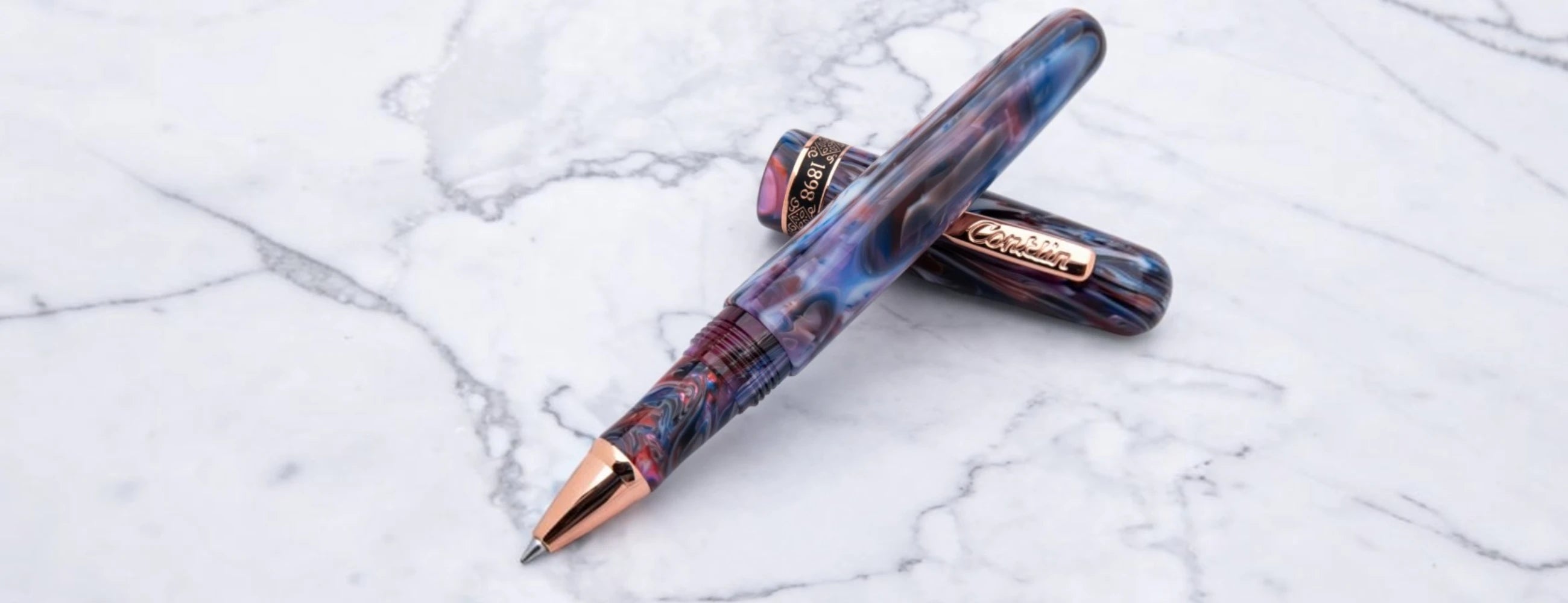 Conklin 1898 rollerball pen with purple and blue marbled barrel on a white marble background.