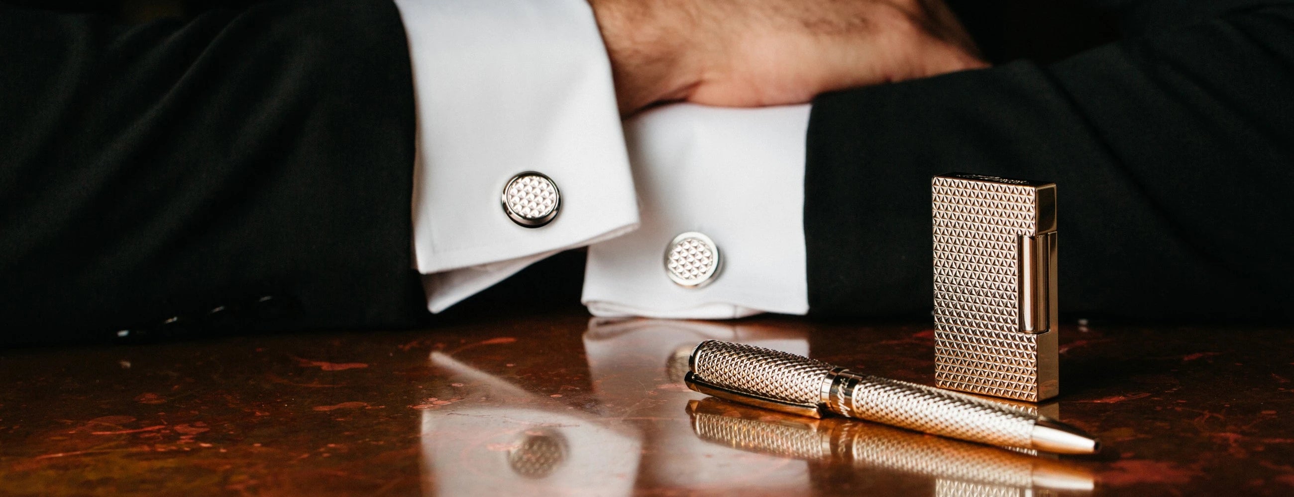 Assortment of S.T. Dupont products with iconic fire head pattern, ballpoint pen, lighter, and matching cufflinks