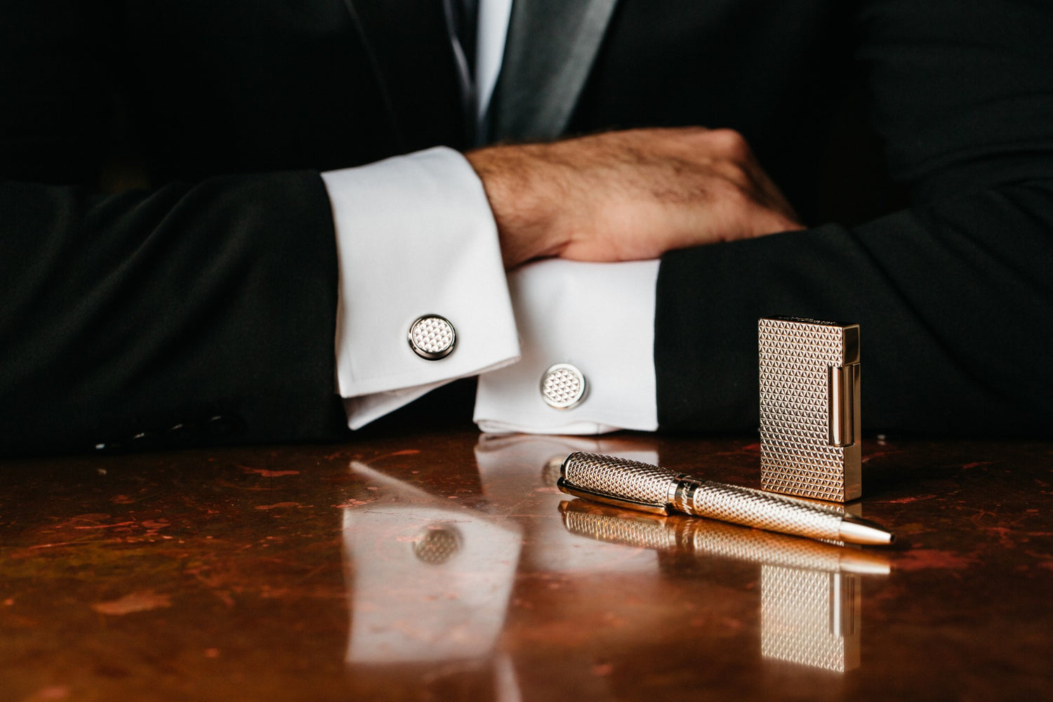 Elegant S.T. Dupont gold lighter and pen set on a reflective table beside a man in a suit with cufflinks