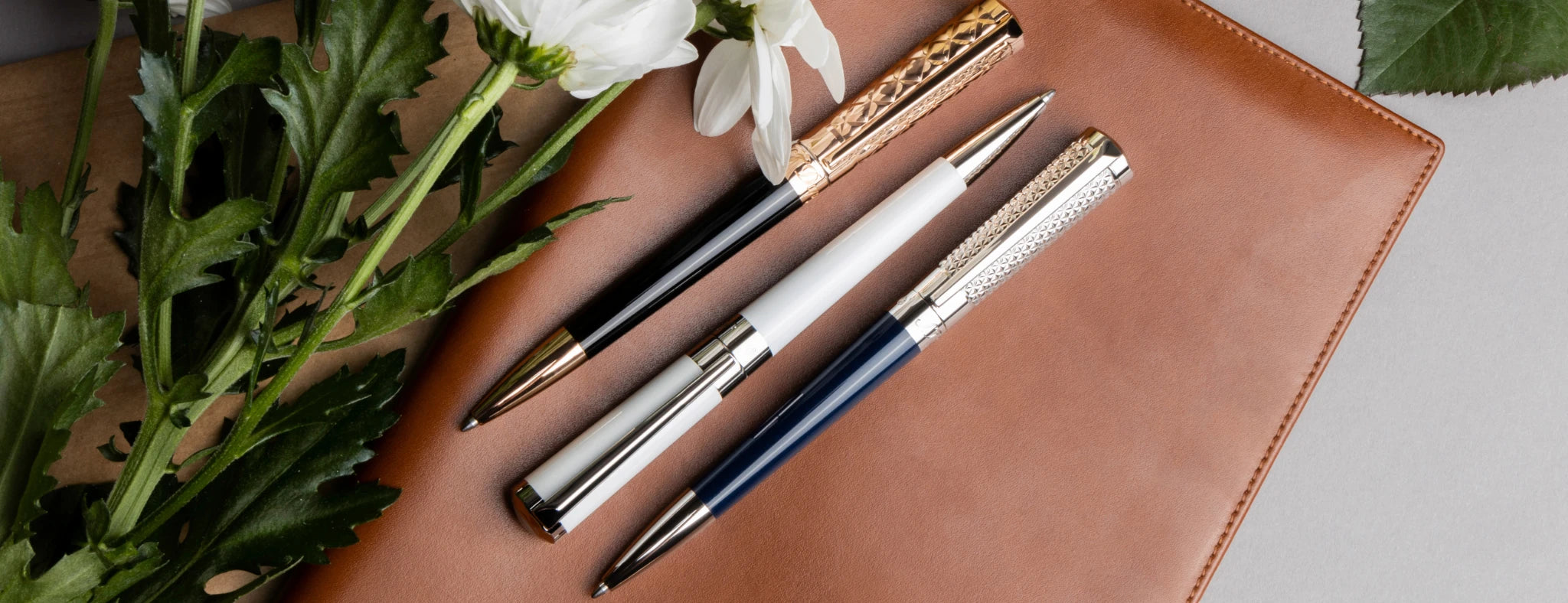 Set of S.T. Dupont Liberte ballpoint pens in white, blue and black lacquer, with palladium and rose gold finish, displayed on leather note book