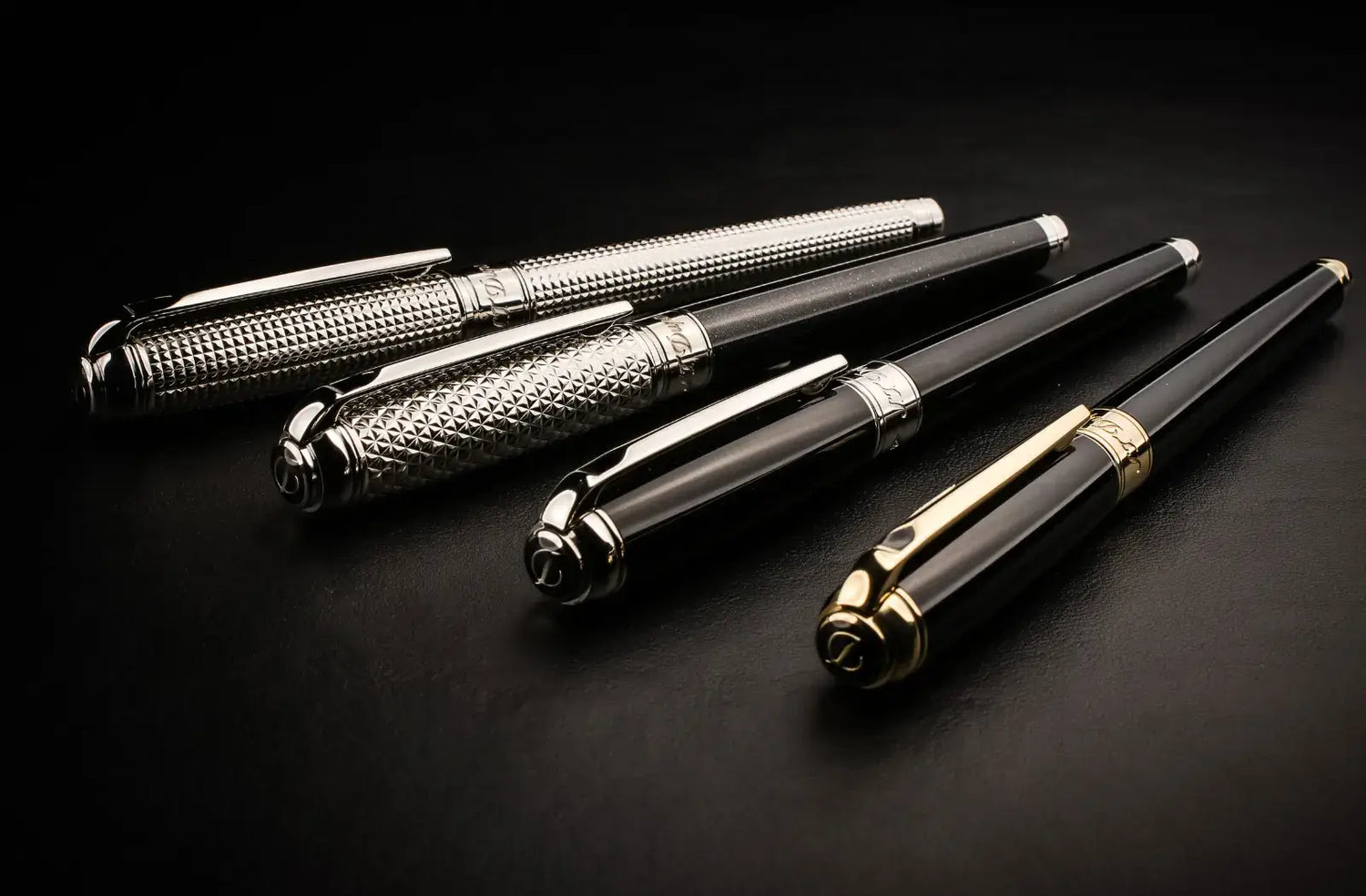 4 S.T. Dupont Line D pens with caps on. Front to back, black lacquer with gold accents, black lacquer with palladium accents, black lacquer with palladium guilloche and palladium guilloche pens