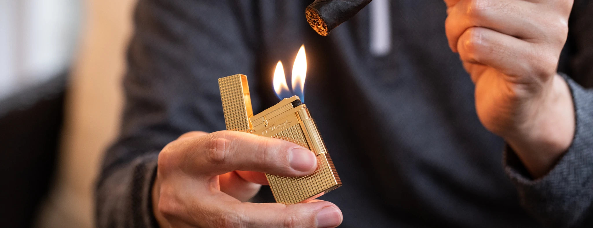 S.T. Dupont Ligne 2 cigar lighter with gold finish and double flame, used to ignite a cigar.