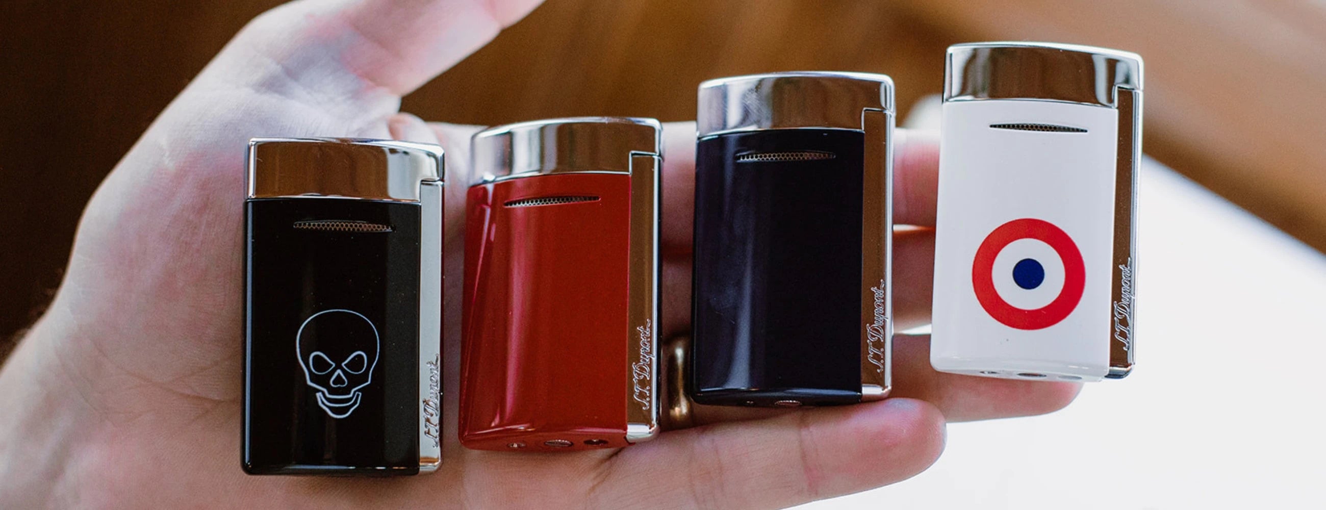 Collection of S.T. Dupont Minijet torch lighters in hand, with red, blue, black or white lacquer and chrome finish.
