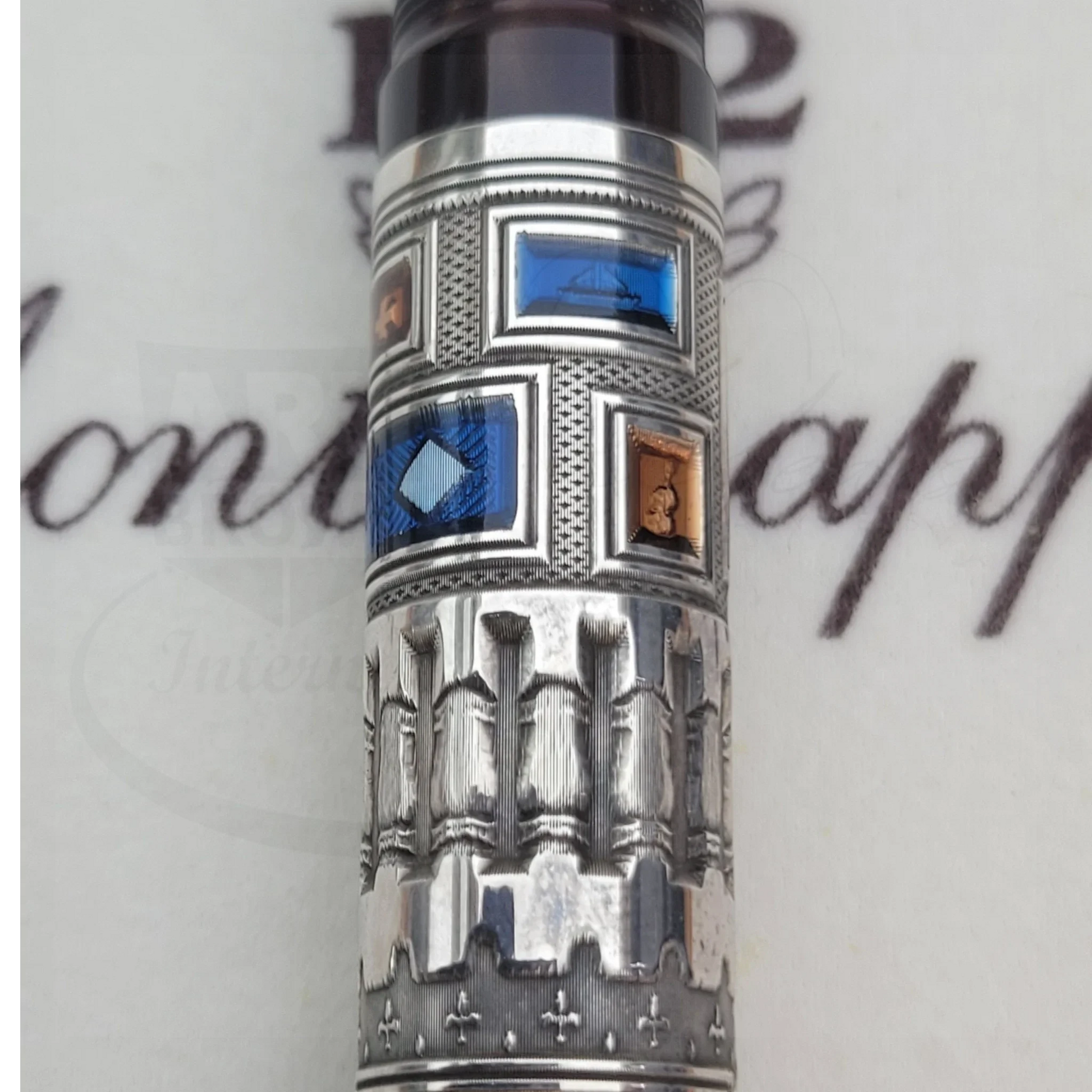 Detailed silver fountain pen barrel with intricate blue and copper guilloche inlays and textured engravings.