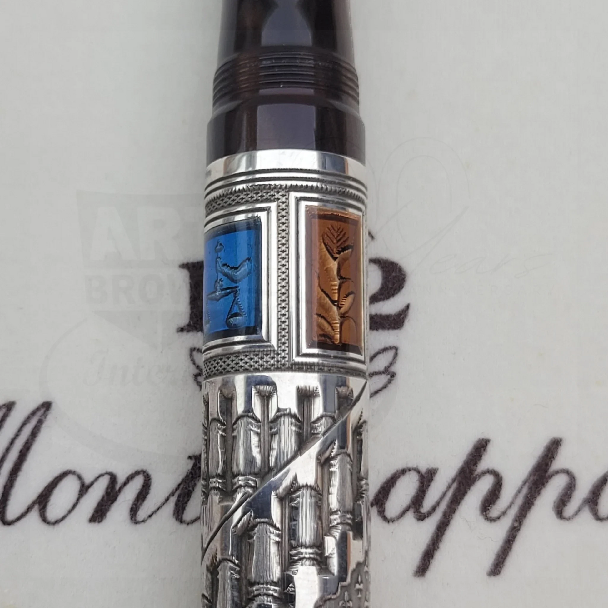 Close-up of a luxury fountain pen with intricate silver guilloche and colored enamel details on the barrel.