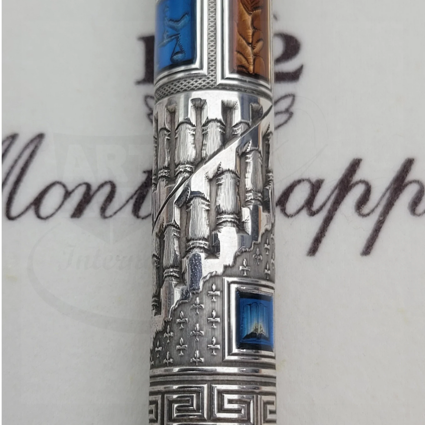 Close-up of an intricately engraved luxury fountain pen barrel with blue and brown inlays and detailed silverwork.