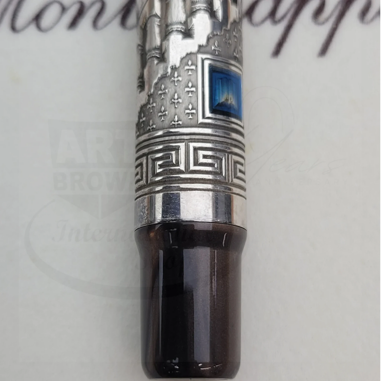 Close-up of a detailed metal fountain pen cap with intricate engravings and a blue gemstone accent.