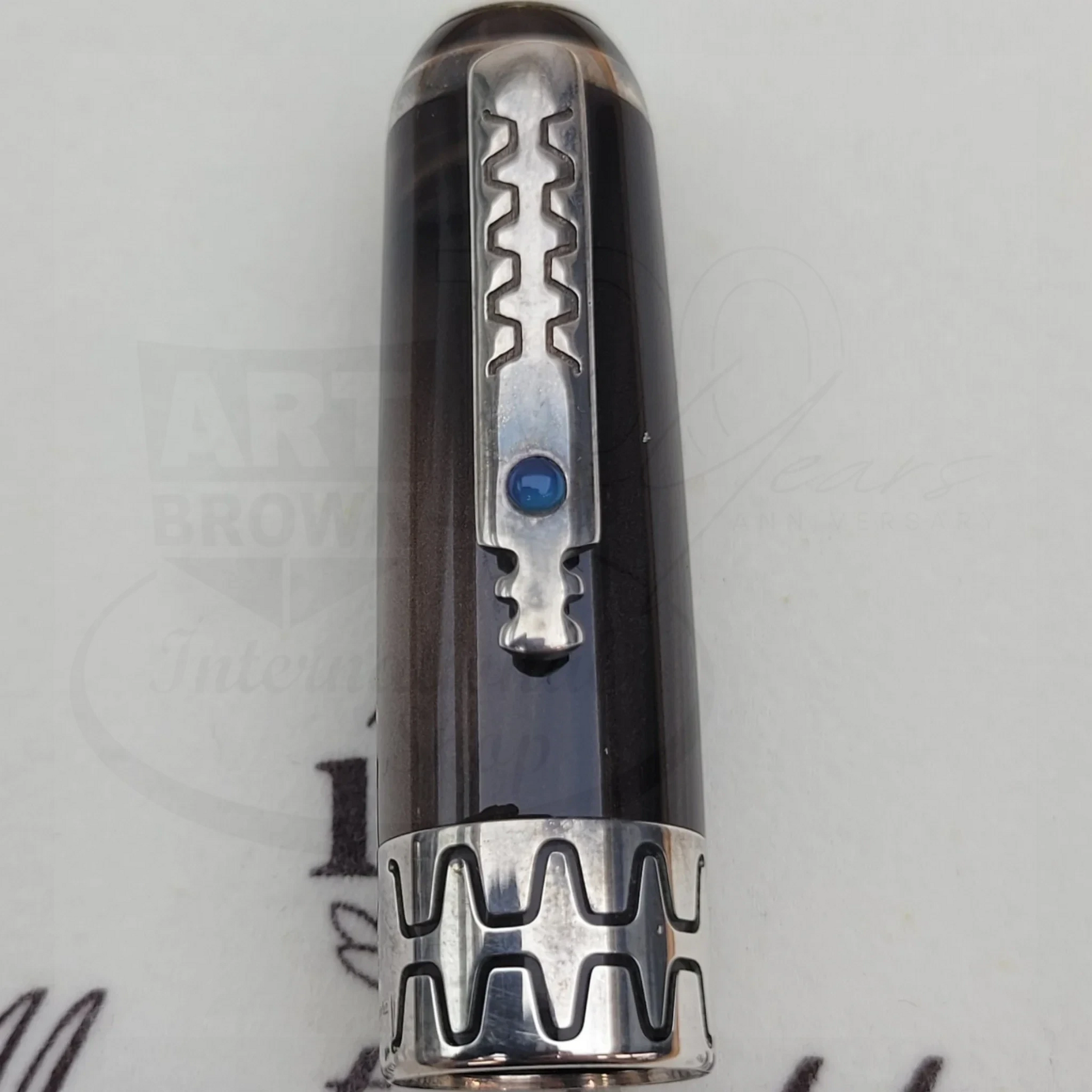 Close-up of a fountain pen cap with intricate silver clip and patterned band featuring a blue gemstone detail.