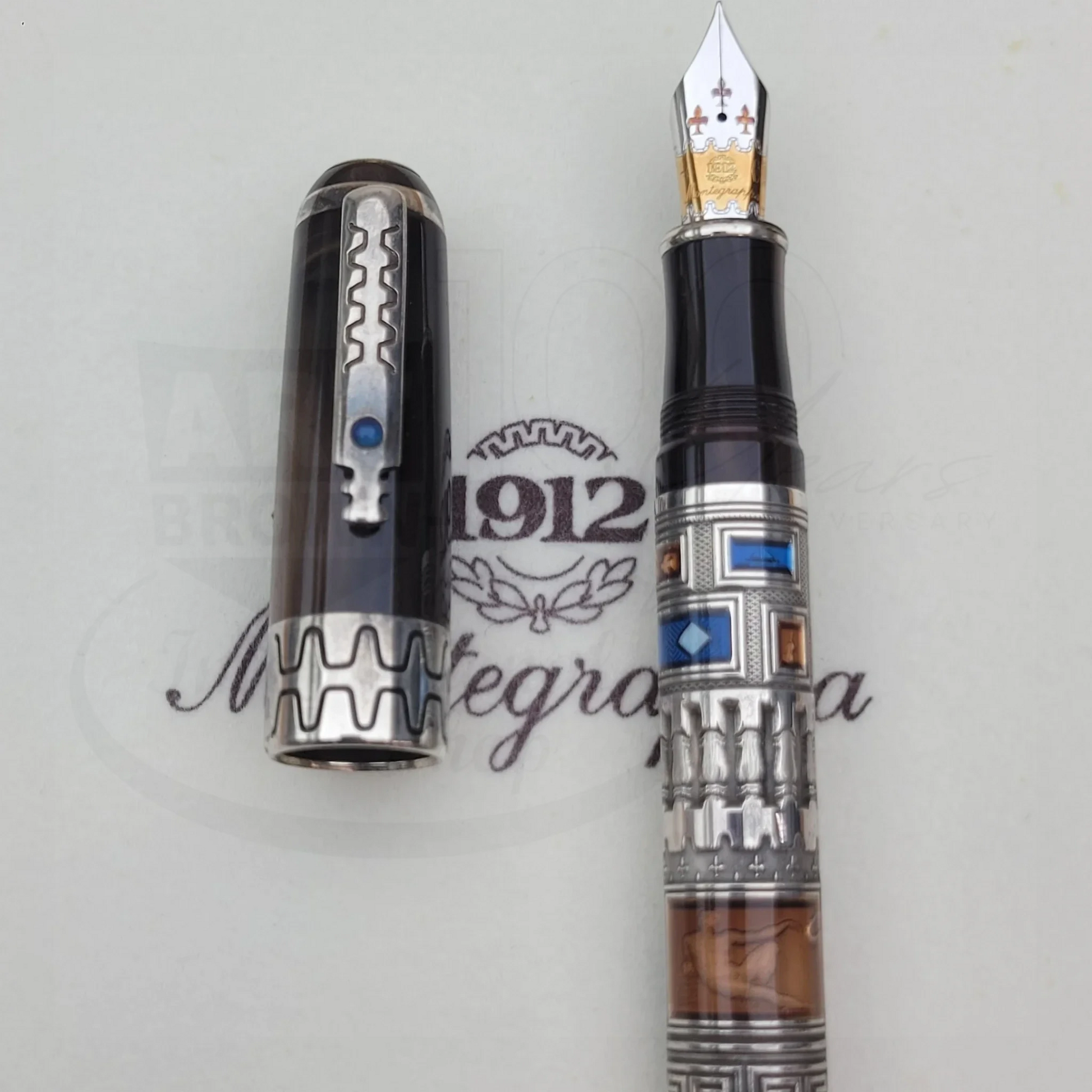 Luxury fountain pen with intricate silver and multicolored geometric design, featuring a detailed nib and cap on branded background.