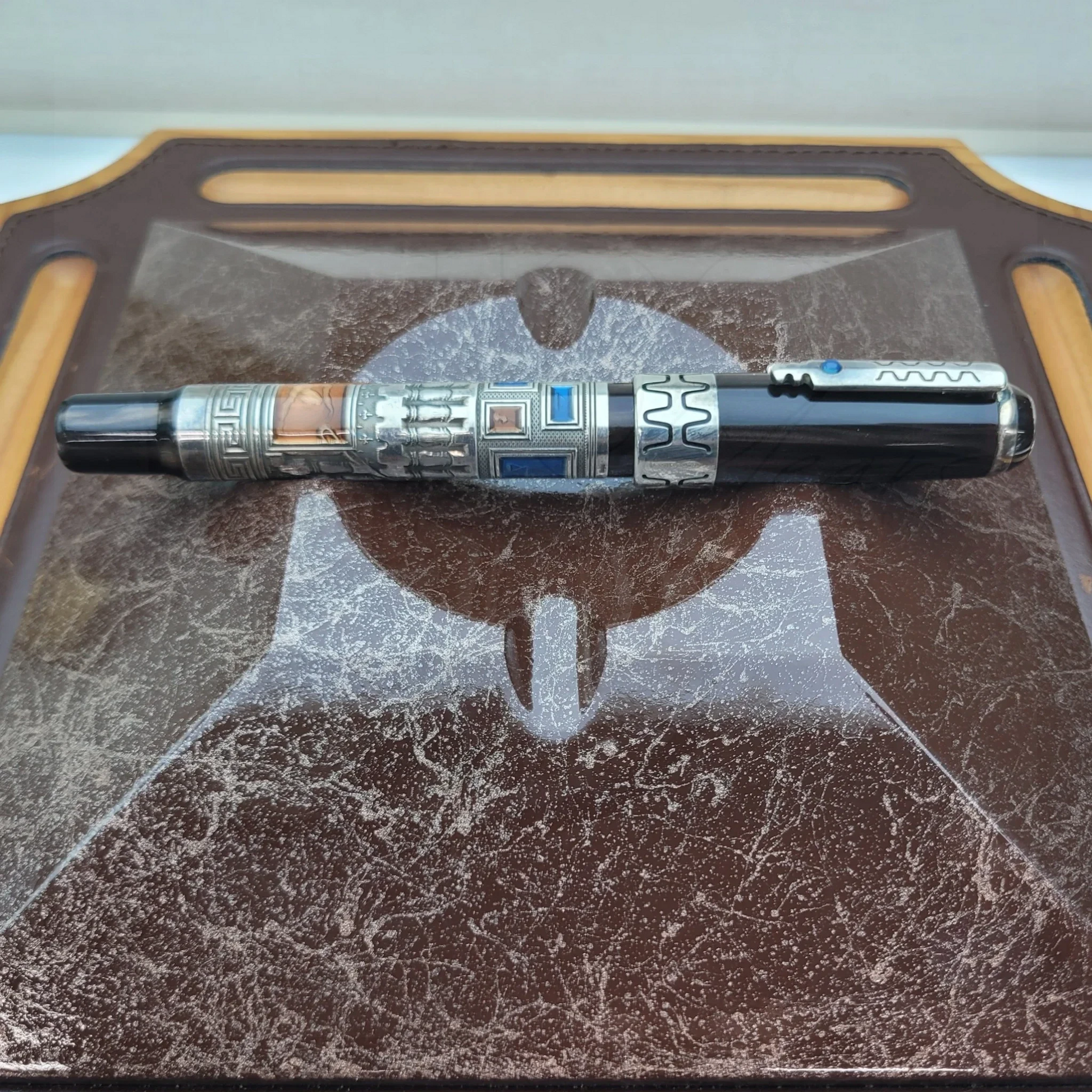 Luxury fountain pen with intricate designs and guilloche detailing resting on a textured leather pen tray