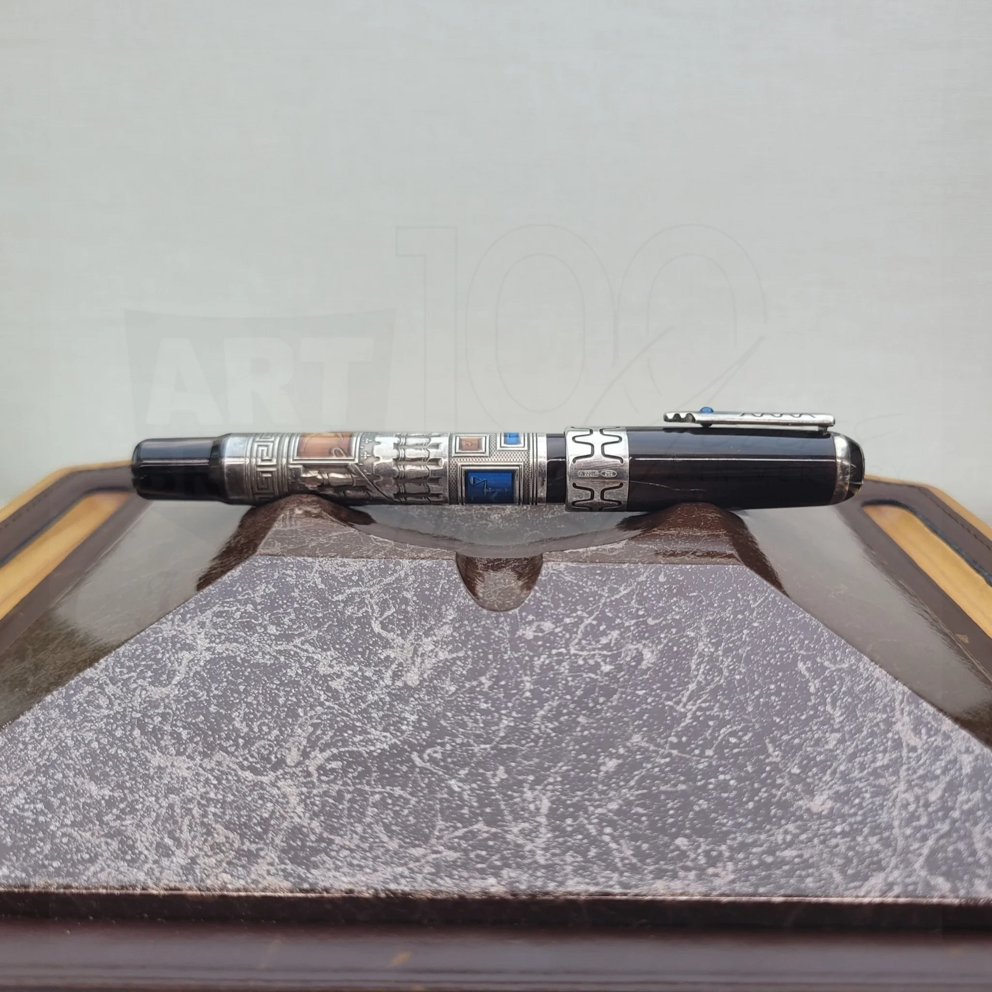 Luxury fountain pen with intricate engravings and silver accents resting on a textured display stand.