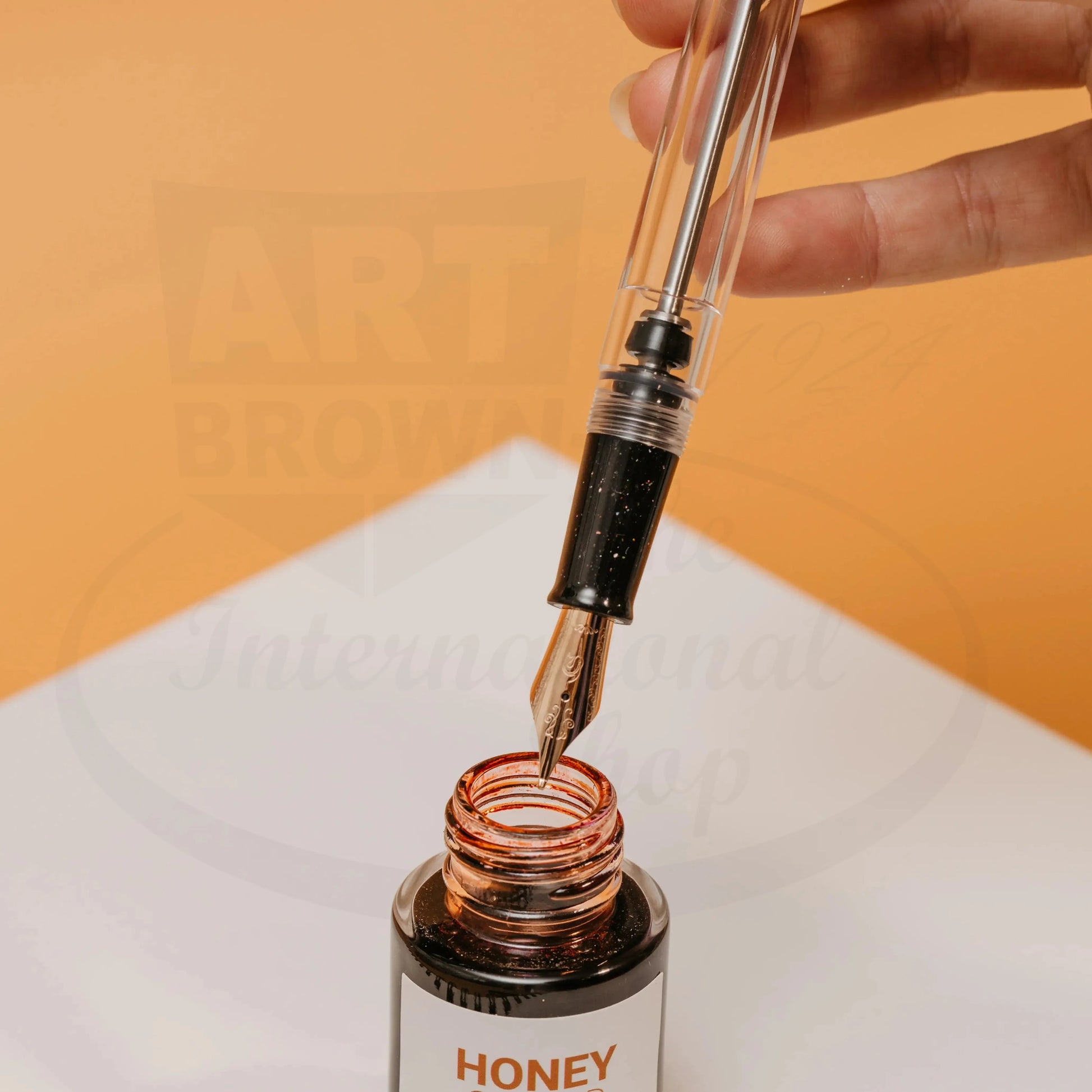 Nahvalur Original Plus Lovina Graphite fountain pen with rose gold nib dipping into honey-colored ink bottle on white surface