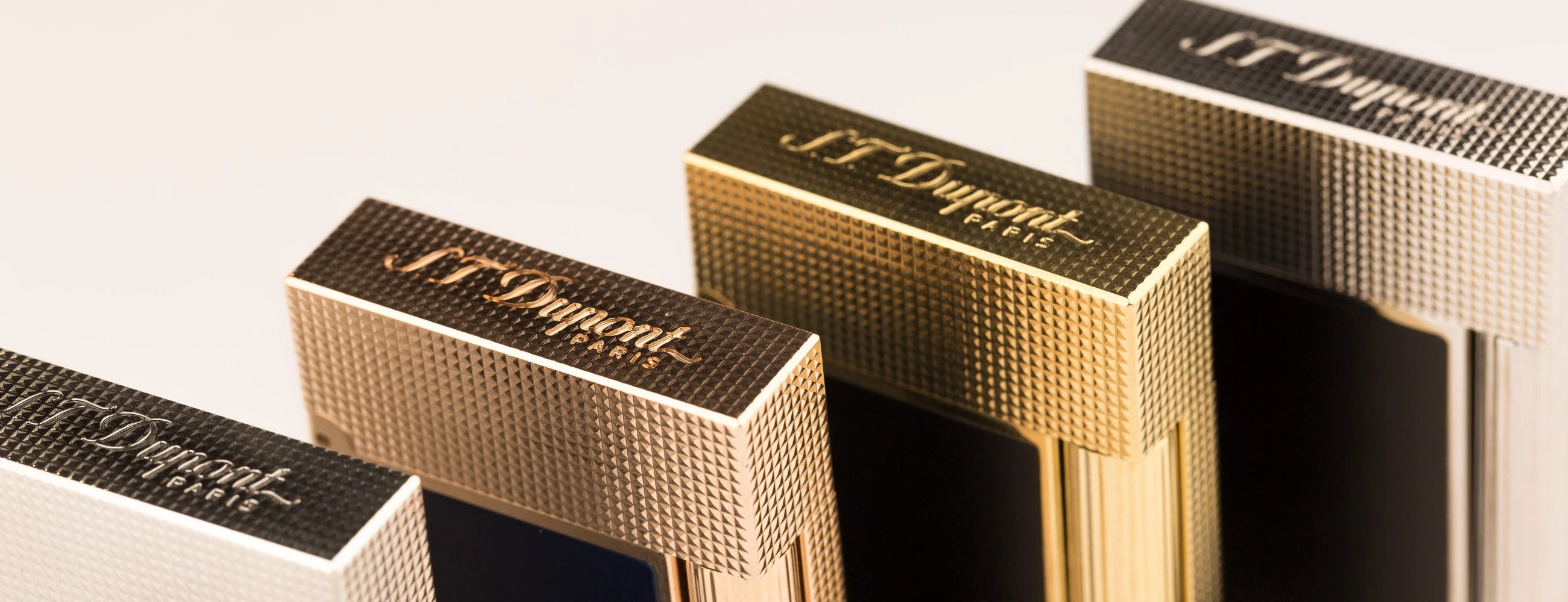 S.T. Dupont perfect ping lighters, showing engraved logo on top of lids with diamond head guilloche, in gold, rose gold, and palladium.