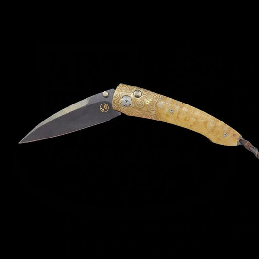 A William Henry B7 knife with the blade partially unfolded, showcasing a Mokume-Gane frame and Tiger Coral handle with a white topaz thumb stud against a black background.