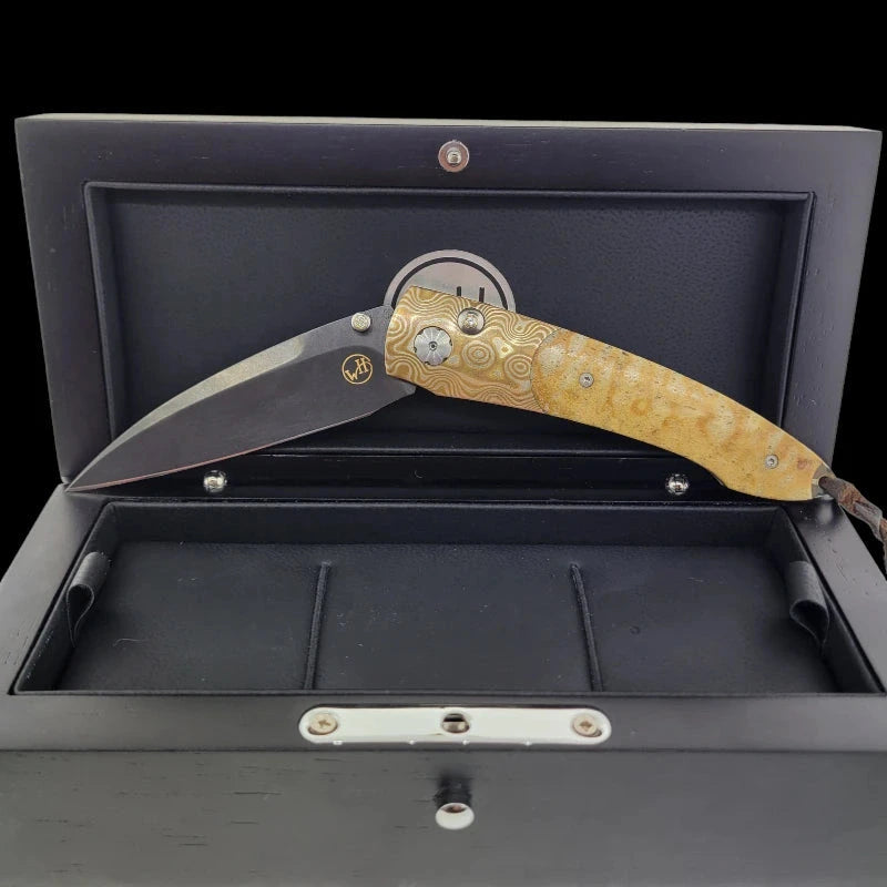Elegant William Henry B7 knife displayed in a partially open position within a luxurious black presentation box, featuring a Tiger Coral handle and Mokume-Gane frame.