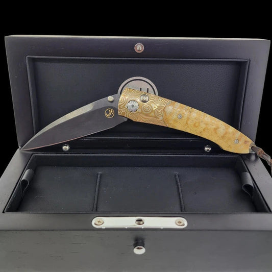 Elegant William Henry B7 knife displayed in a partially open position within a luxurious black presentation box, featuring a Tiger Coral handle and Mokume-Gane frame.