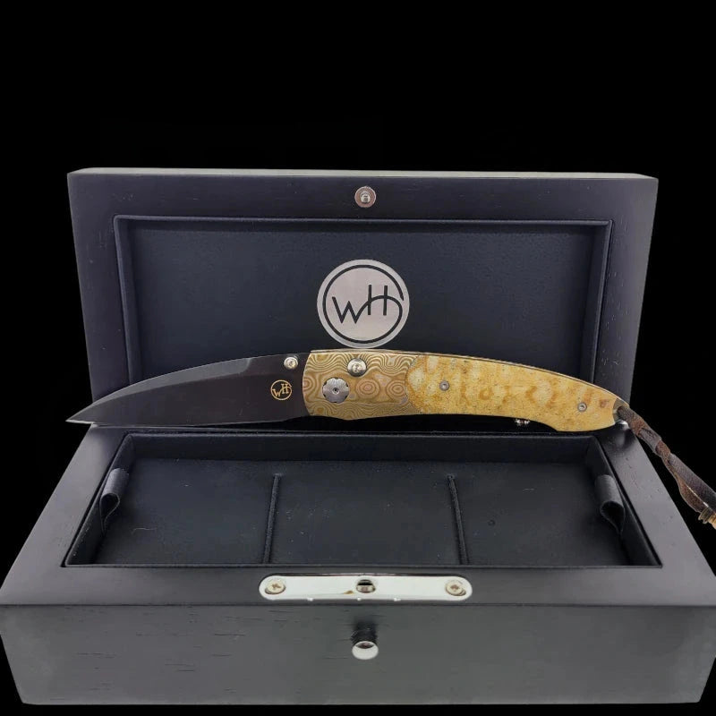 William Henry B7 knife displayed fully open in a presentation box, showing the ATS-34 steel blade coated with black boron and Tiger Coral handle.